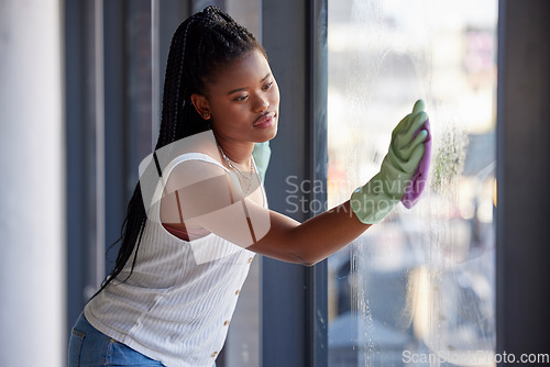 Image of Housework, hygiene and black woman cleaning the window with cloth while doing housekeeping. Cleaning service, routine and African female cleaner, maid or housewife washing glass door for dust or dirt