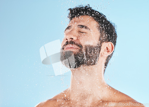 Image of Man shower, cleaning face and studio for self care wellness, relax and beauty by blue background. Model, skincare and water drop on facial, beard and self love for health, body or clean by backdrop