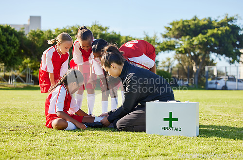 Image of Sports, first aid and children soccer team with an injury after a game in a huddle helping a girl athlete. Fitness, training and kid with a sore, pain or muscle sprain on an outdoor football field.