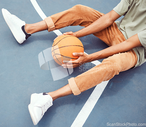 Image of Basketball, hands and fitness with a sports man sitting alone on a court, holding a ball from above. Basketball court, break and exercise with a male basketball player or athlete resting at practice