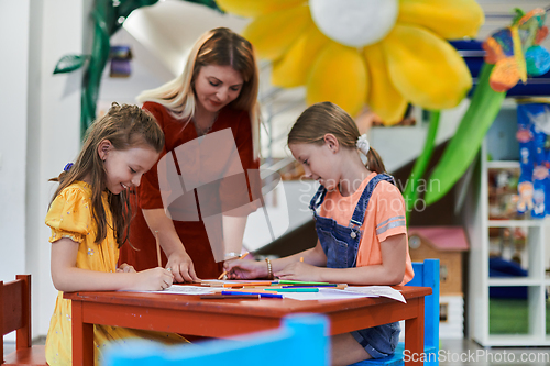 Image of Creative kids during an art class in a daycare center or elementary school classroom drawing with female teacher.