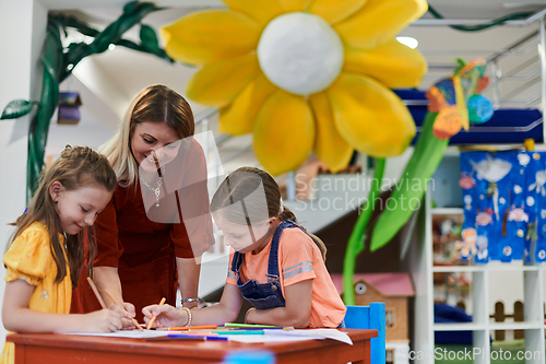 Image of Creative kids during an art class in a daycare center or elementary school classroom drawing with female teacher.