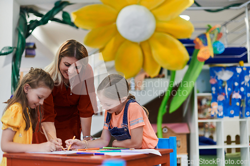 Image of Creative kids during an art class in a daycare center or elementary school classroom drawing with female teacher.