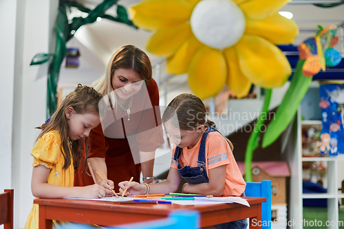 Image of Creative kids during an art class in a daycare center or elementary school classroom drawing with female teacher.