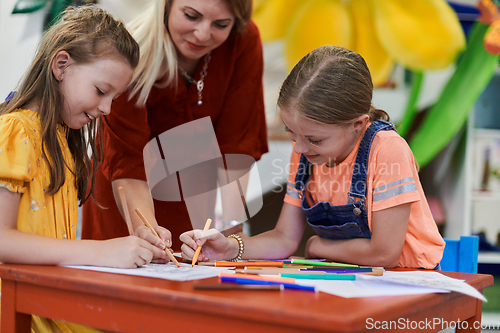 Image of Creative kids during an art class in a daycare center or elementary school classroom drawing with female teacher.