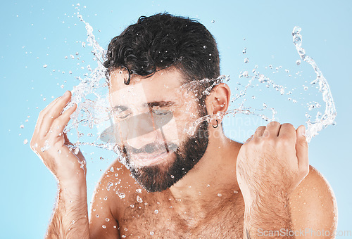 Image of Man, cleaning and beauty with splash in studio for health, self care and smile by blue background. Model, skincare and water with clean for healthy facial, self love and cosmetics by studio backdrop