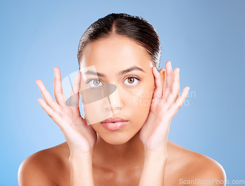 Image of Face portrait, skincare and beauty of woman in studio on a blue background. Hands, natural cosmetics and makeup of young female model with healthy, smooth and glowing skin after facial treatment.