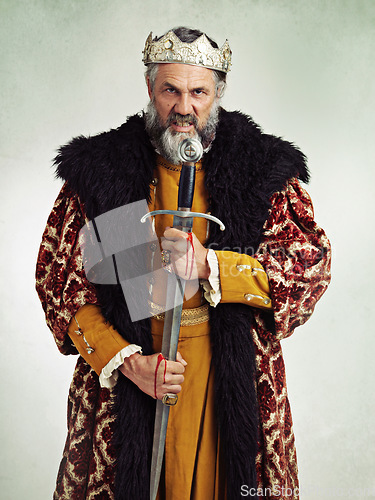 Image of King, angry and portrait of man with sword in studio isolated on a gray background. Victorian royalty, evil and mad senior male, annoyed ruler and frustrated leader holding bloody blade after battle.