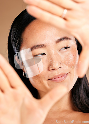 Image of Asian woman, hand frame and studio for skincare, natural skin glow and smile with cosmetics for health. Japanese model, cosmetic beauty and healthy aesthetic for self care, wellness or happy headshot