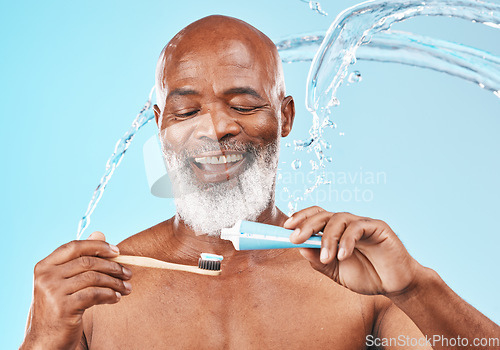 Image of Water, splash and man with dental care in a studio for mouth health and wellness. Toothpaste, toothbrush and elderly African guy brushing his teeth for fresh oral hygiene isolated by blue background.