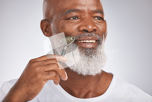 Image of Black man, facial roller and skincare to massage skin for self care with dermatology beauty tool. Headshot of a happy senior male with a stone on grey studio background for spa treatment for the face