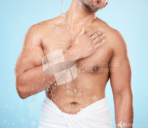 Image of Body, water and shower with a man model standing in studio on a blue background for hygiene or hydration. Splash, health and wellness with a male wearing a towel in the bathroom after bathing