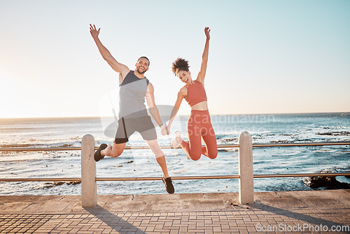 Image of Fitness, jump and portrait of a couple at beach for training fun, support and celebration of goal. Energy, happy and excited man and woman jumping while holding hands at the sea for cardio in Spain