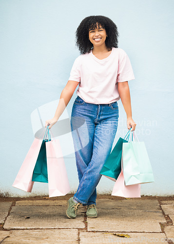 Image of Shopping, retail and portrait of a woman with bags from a sale on a blue city wall in Greece. Fashion, product and girl shopper carrying content from a shop, boutique or store downtown with a smile