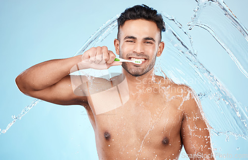 Image of Face, water splash and man with toothbrush for cleaning in studio on blue background. Dental veneers, hygiene and portrait of happy male model brushing teeth for oral wellness, health or fresh breath