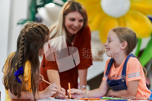 Image of Creative kids during an art class in a daycare center or elementary school classroom drawing with female teacher.