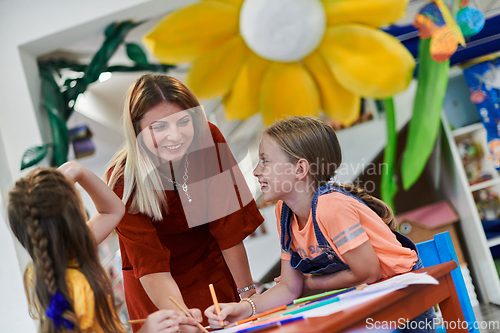 Image of Creative kids during an art class in a daycare center or elementary school classroom drawing with female teacher.