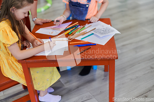 Image of Creative kids during an art class in a daycare center or elementary school classroom drawing with female teacher.