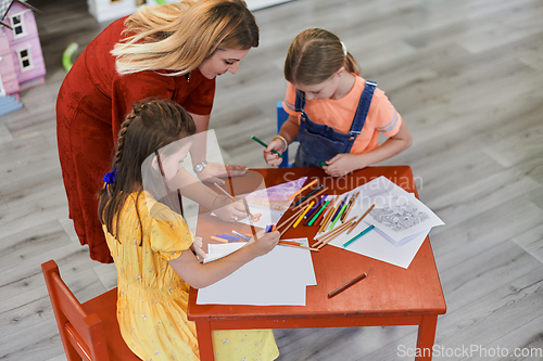 Image of Creative kids during an art class in a daycare center or elementary school classroom drawing with female teacher.