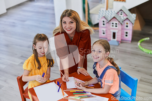 Image of Creative kids during an art class in a daycare center or elementary school classroom drawing with female teacher.