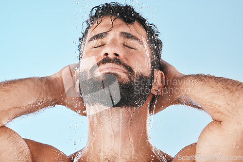 Image of Face, water splash and man in shower for skincare in studio isolated on a blue background. Dermatology, water drops and male model cleaning, bathing or washing for healthy skin, hygiene and wellness.