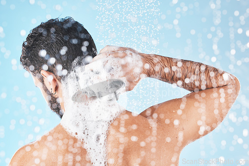 Image of Shower, water and man with soap for cleaning, washing and hygiene on blue background in studio. Grooming, bathroom and back of male with foam, sponge and water splash for skincare, wellness and spa