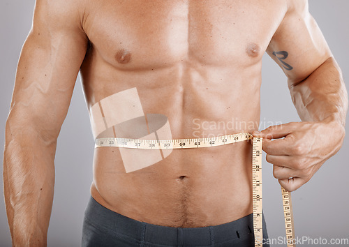 Image of Man, body and tape measure on abdomen in studio on gray background. Health, fitness and male model with measuring tape for abs to track exercise training results, muscle goals or weight loss target.