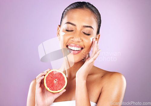 Image of Woman, face skincare or grapefruit cream on purple studio background in organic dermatology, healthcare sunscreen wellness or self care grooming. Smile, happy or beauty model and fruit facial product