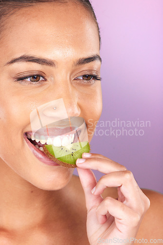 Image of Woman, face and kiwi for skincare beauty wellness, natural cosmetics health and fruit nutrition diet on purple studio background. Model eating, vitamin c and smile for organic facial skin glow vision