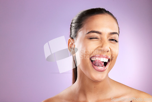 Image of Woman, tongue and wink for skincare wellness or face dermatology beauty in purple studio background. Model, sily facial cosmetics care and natural glowing skin or comic happiness or headshot vision