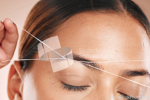 Image of Eyebrows, grooming and woman threading hair on face for beauty routine, shaping and cosmetics care on a studio background. Zoom, trimming and cosmetic model cleaning facial hair with a thread