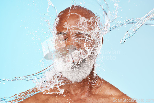 Image of Elderly black man, water splash and face in studio for wellness, clean or facial health by backdrop. Man, model face and water for skincare, healthy self care or cosmetic beauty by blue background