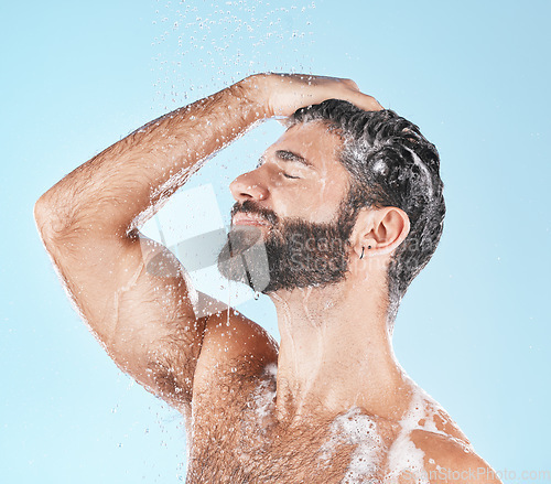 Image of Face, water splash and shampoo shower of man in studio isolated on a blue background. Water drops, hair care hygiene and male model washing, cleaning or bathing for healthy skin, wellness or skincare