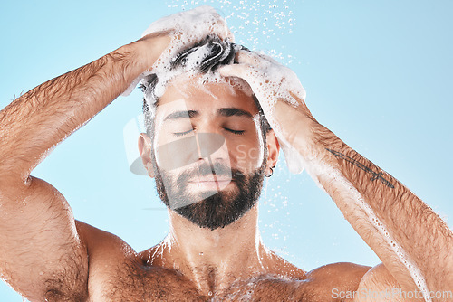 Image of Hair care, face water splash and shower of man in studio isolated on a blue background. Water drops, shampoo and male model washing, cleaning or bathing for healthy skin, wellness or skincare hygiene