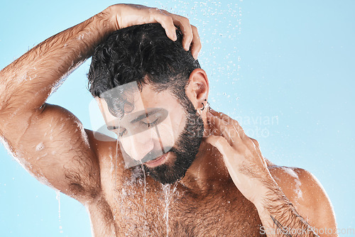 Image of Hair care, face and water splash of man in shower in studio isolated on a blue background. Water drops, dermatology and male model washing, cleaning or bathing for skincare, wellness and hygiene.