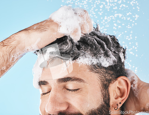 Image of Face, water splash and man in shower with shampoo in studio on a blue background. Skincare dermatology, water drops and male model cleaning, bathing or washing for hair care, hygiene and wellness.