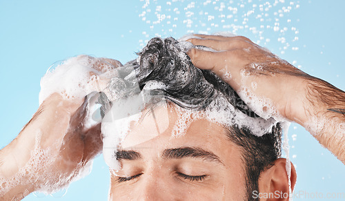 Image of Face, water splash and shampoo shower of man in studio isolated on a blue background. Water drops, hair care and male model washing, bathing or cleaning for healthy skin, wellness or skincare hygiene