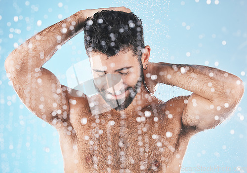 Image of Face, water splash and skincare shower of man in studio isolated on a blue background. Dermatology, water drops and male model bathing, washing or cleaning for hygiene, wellness and healthy skin.