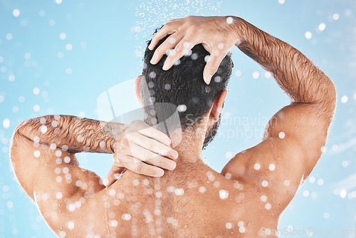 Image of Face, back and water splash of man in shower in studio on a blue background. Water drops, dermatology and male model washing, cleaning or bathing for fresh hygiene, skincare wellness or healthy skin.