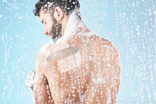 Image of Shower, water and man with soap for cleaning, washing and hygiene on blue background in studio. Grooming, bathroom and back of male with foam, sponge and water splash for skincare, wellness and spa