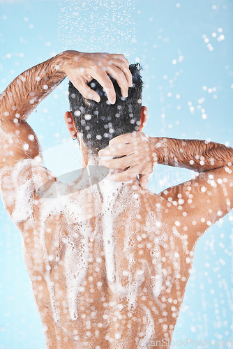 Image of Shower, water and man cleaning body with soap, foam and hair products on blue background in studio. Bathroom hygiene, grooming and back of male washing body for self care, spa wellness and skincare