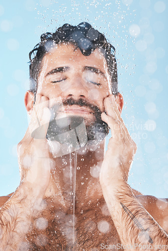 Image of Face, skincare shower and water splash of man in studio isolated on a blue background. Water drops, dermatology and male model washing, cleaning or bathing for healthy skin, wellness and hygiene.