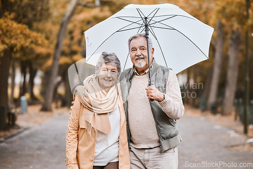 Image of Winter, hug and senior couple in a park, retirement date and walking in Canada with an umbrella. Nature affection, smile and portrait of an elderly man and woman on a walk for happiness and love