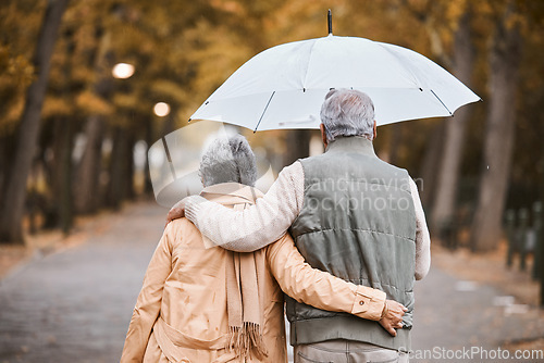 Image of Elderly, couple walk in park with umbrella and fresh air, outdoor in nature in fall for exercise and retirement together. Hug, love and care with trees, senior man and woman in New York back view.