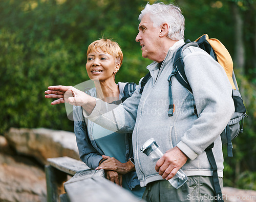 Image of Couple, elderly and hiking in forest with fitness and interracial, talking about view and relax while trekking. Retirement, exercise and hike in nature with water bottle for hydration and travel.