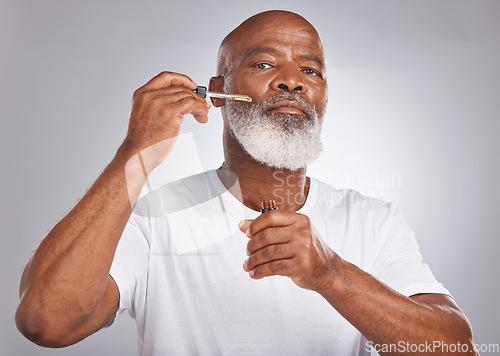 Image of Senior man, face serum and skincare with dermatology and cosmetics for clean, glow and fresh skin. Portrait of a black male with a pipette for collagen oil on a grey studio background for beauty