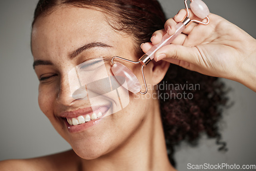 Image of Woman, face and smile with roller for skincare cosmetics, beauty or self love and care against grey studio background. Closeup of female smiling with rolling tool in satisfaction for makeup treatment