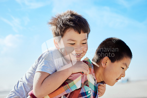 Image of Asian kids, siblings and piggyback on the beach for fun summer vacation together in the outdoors. Happy Japanese children with smile playing by the ocean coast on a back ride on a warm sunny day