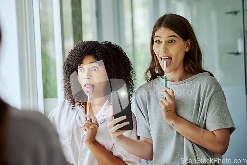 Image of Friends, wellness and brushing teeth phone selfie with crazy face for morning hygiene routine in home. Comic, goofy and interracial friendship of women cleaning teeth with smartphone photograph.