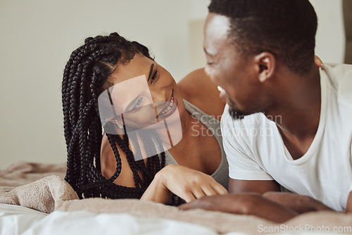 Image of Black couple, love and home bedroom bonding while happy together on a bed at home, apartment or hotel for honeymoon. Young man and woman talking while in a happy marriage with communication and care